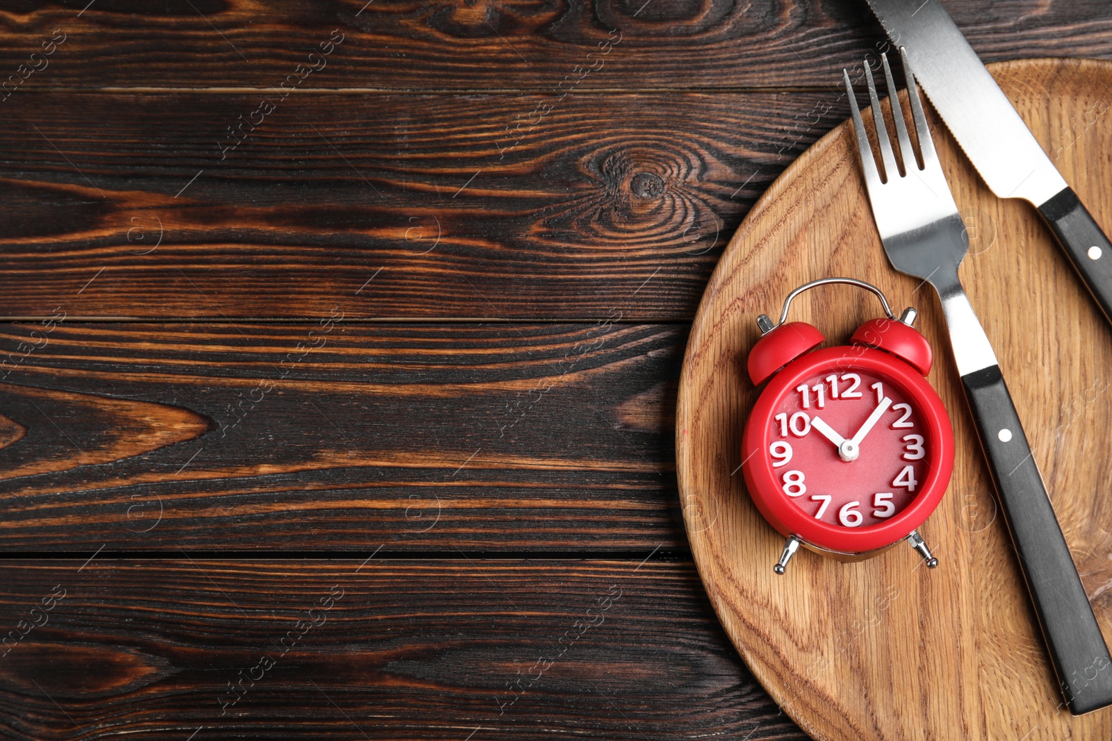Photo of Alarm clock and cutlery in plate on wooden table, top view with space for text. Diet regime