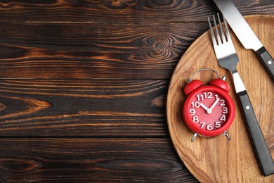 Alarm clock and cutlery in plate on wooden table, top view with space for text. Diet regime