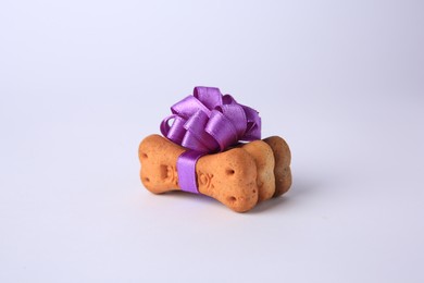 Photo of Bone shaped dog cookies with purple bow on white background