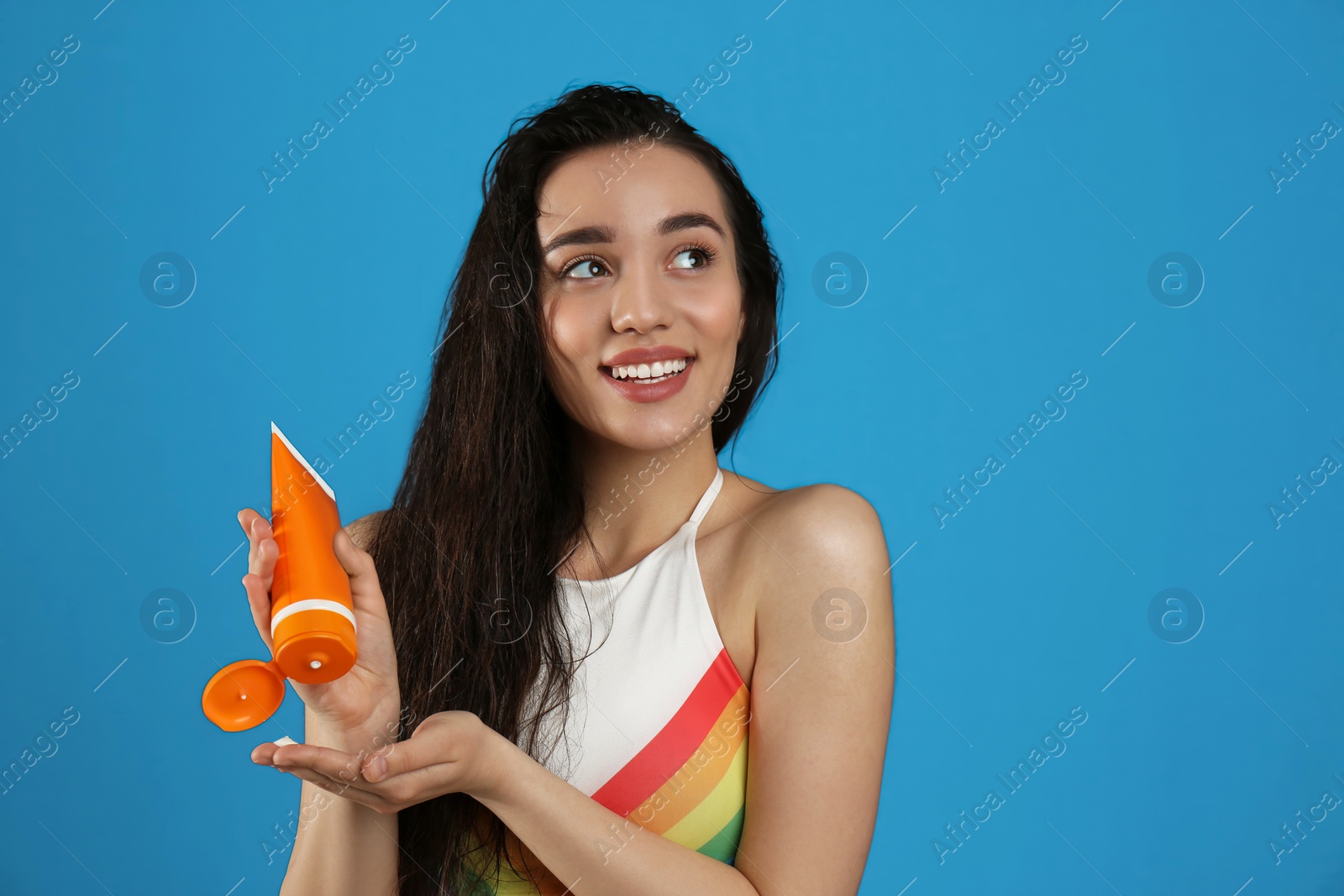 Photo of Young woman applying sun protection cream on dark blue background