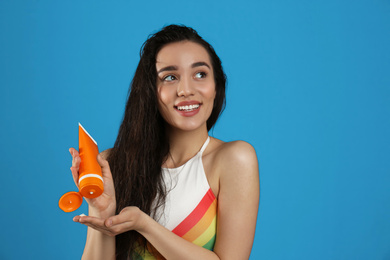 Photo of Young woman applying sun protection cream on dark blue background