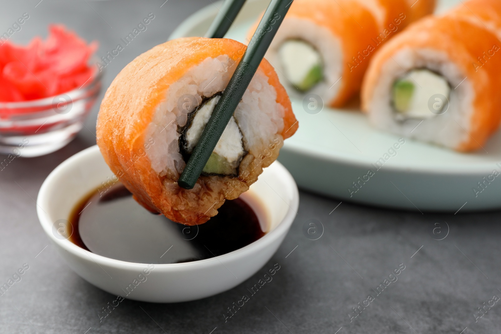 Photo of Dipping tasty sushi into soy sauce at grey table, closeup