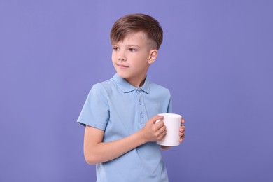 Photo of Cute boy with white ceramic mug on violet background