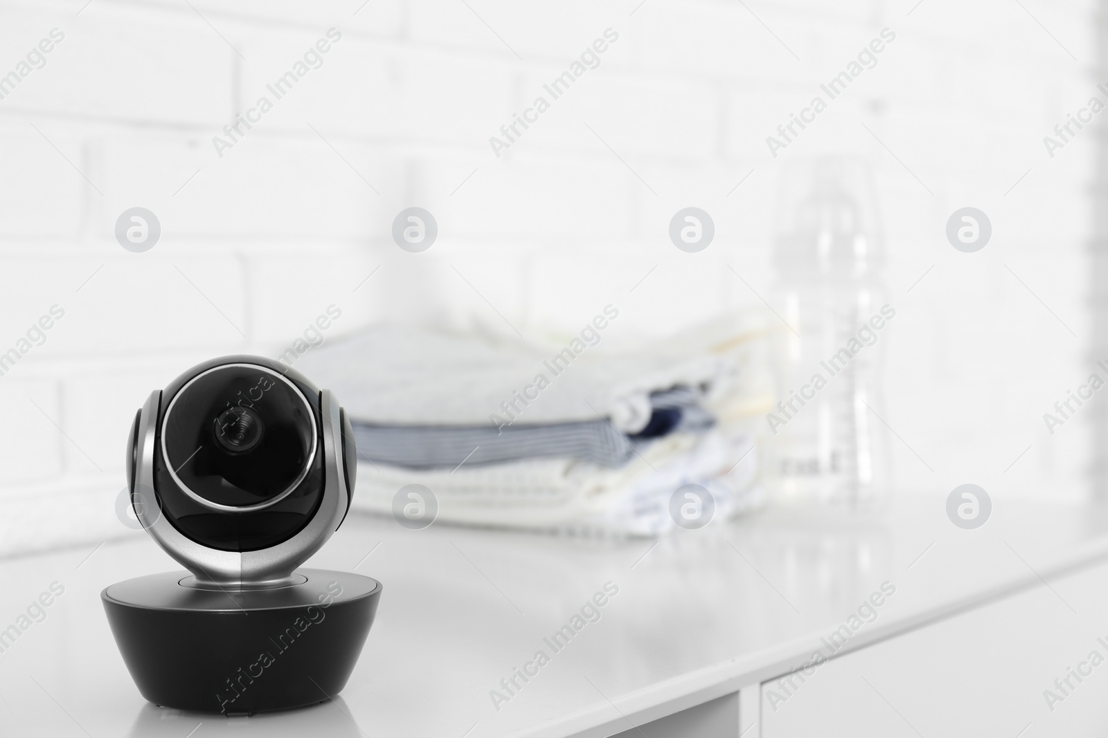 Photo of Baby camera on table near white brick wall, space for text. Video nanny