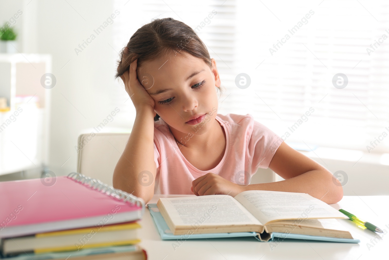 Photo of Sad little girl doing homework at table indoors