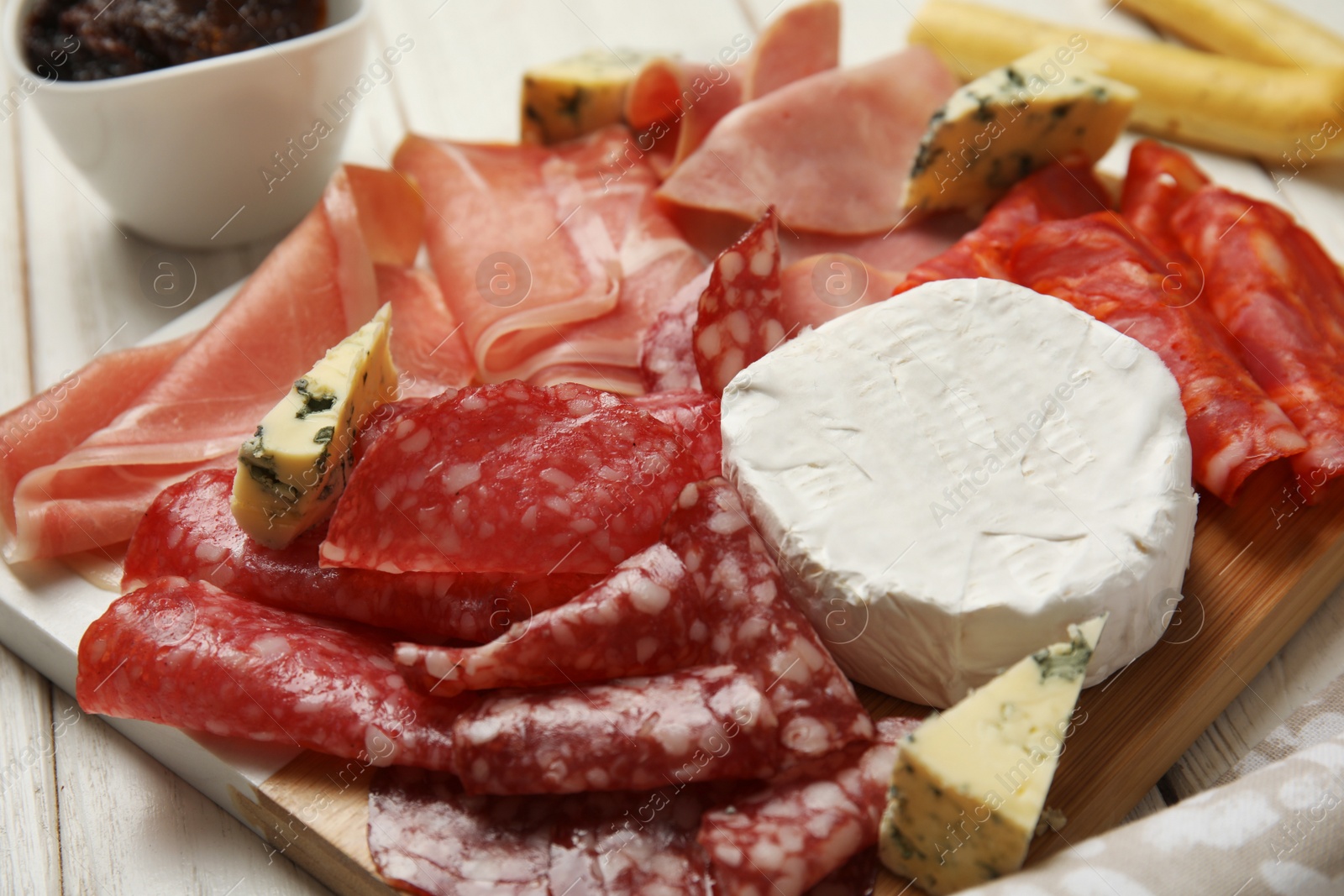 Photo of Tasty ham with other delicacies served on white wooden table, closeup