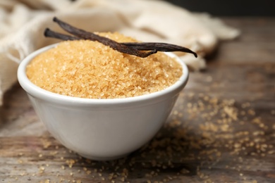 Photo of Bowl of aromatic vanilla sugar and sticks on wooden background