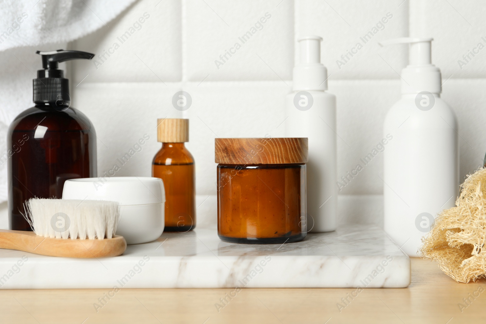 Photo of Different bath accessories and personal care products on wooden table near white tiled wall