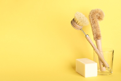 Photo of Cleaning brushes and soap bar on yellow background, space for text. Dish washing supplies