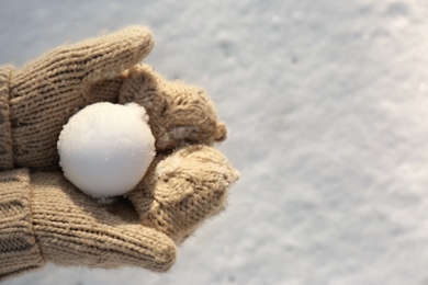 Photo of Woman in knitted mittens holding snowball outdoors, closeup. Space for text