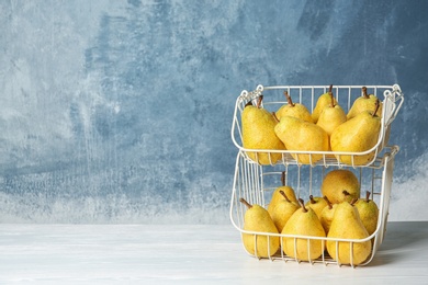 Photo of Basket of fresh ripe pears on table against color background with space for text