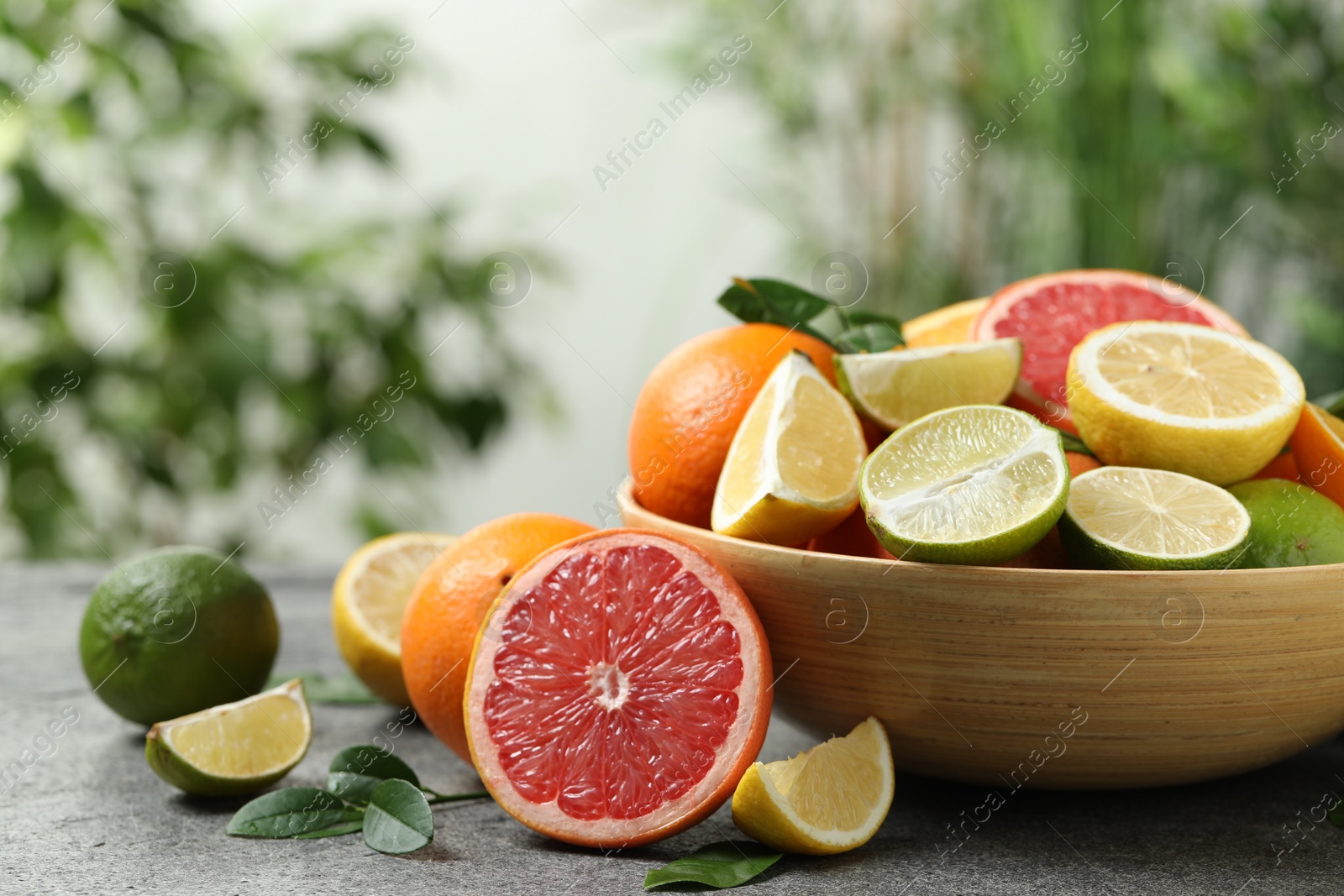 Photo of Different fresh citrus fruits and leaves on table against blurred background, closeup