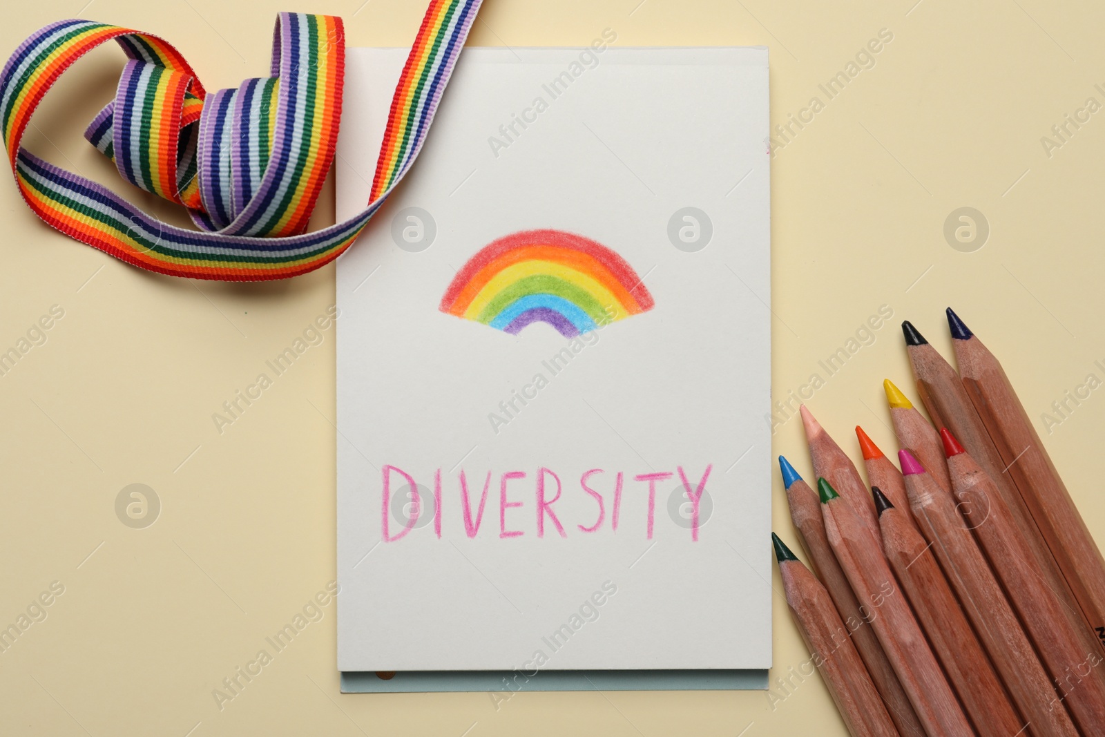 Photo of Paper sheet with word Diversity and rainbow, pencils, ribbon on beige background, flat lay