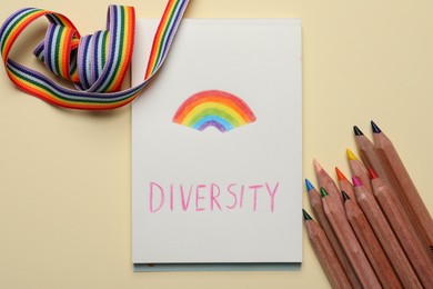 Paper sheet with word Diversity and rainbow, pencils, ribbon on beige background, flat lay