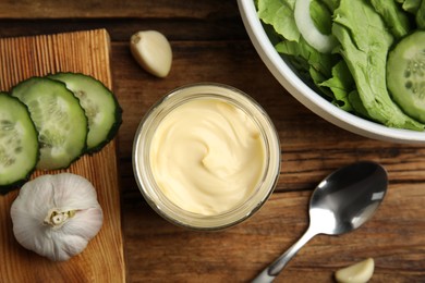 Photo of Jar of delicious mayonnaise, salad and vegetables on wooden table, flat lay