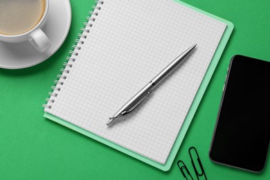 Ballpoint pen, notebook and smartphone on green background, flat lay