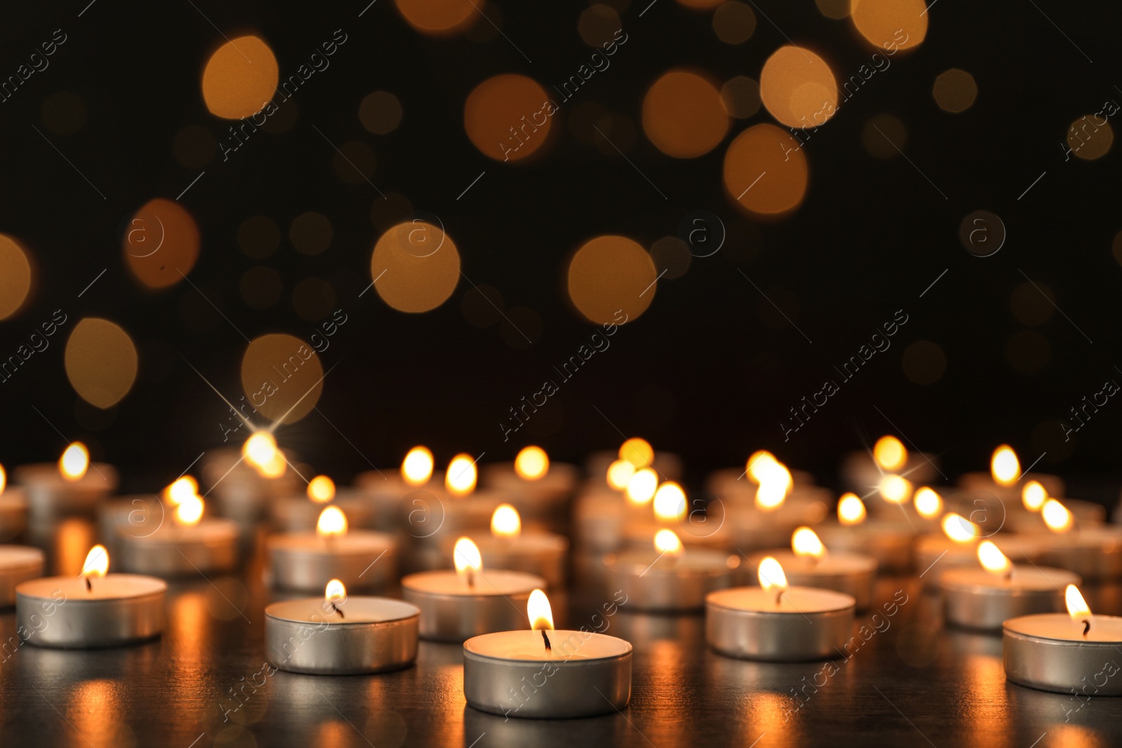 Image of Many burning candles on table against dark background with blurred lights. Bokeh effect