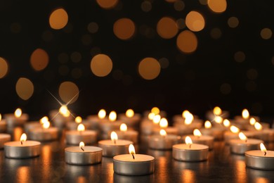 Image of Many burning candles on table against dark background with blurred lights. Bokeh effect