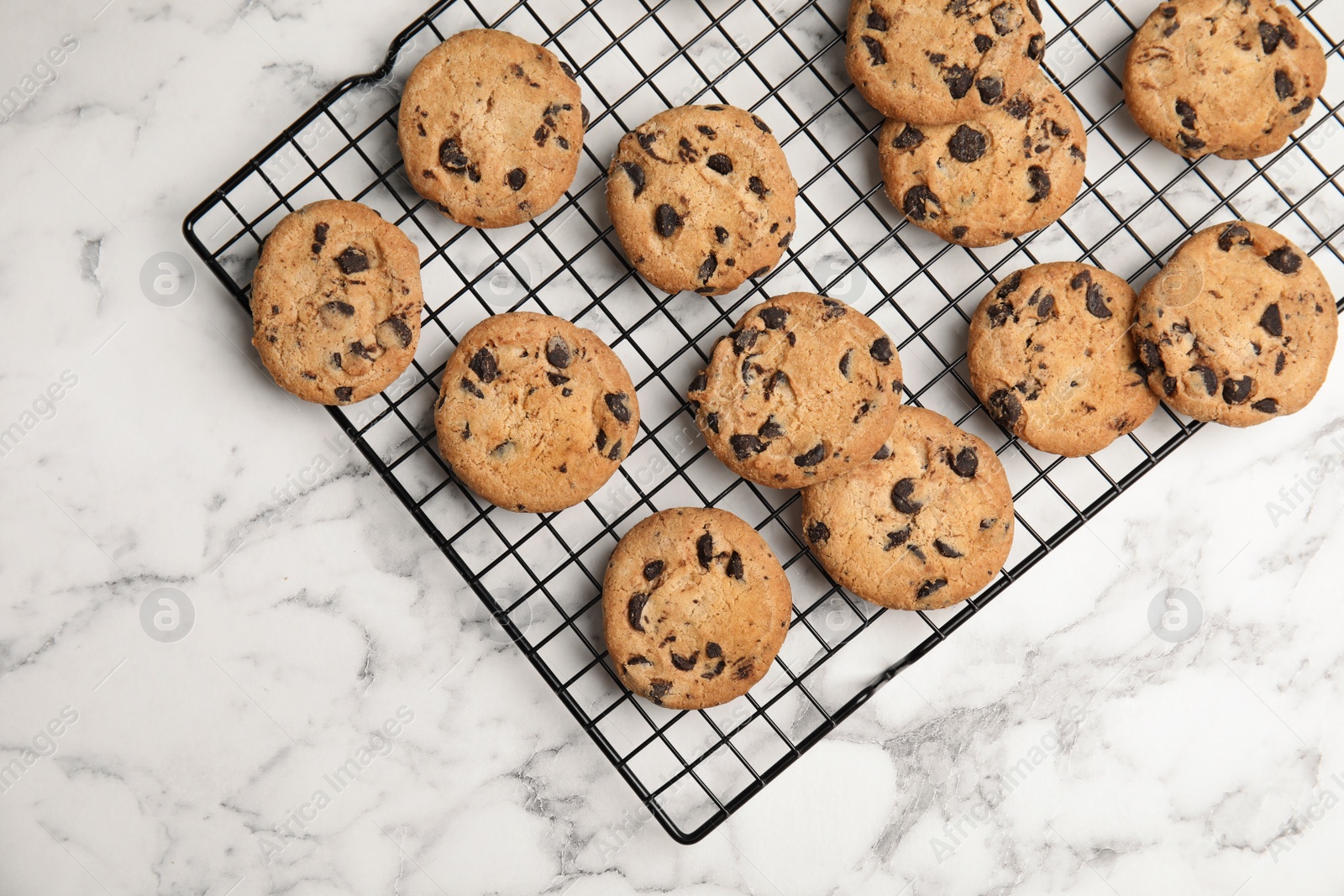 Photo of Cooling rack with chocolate chip cookies on marble background, top view