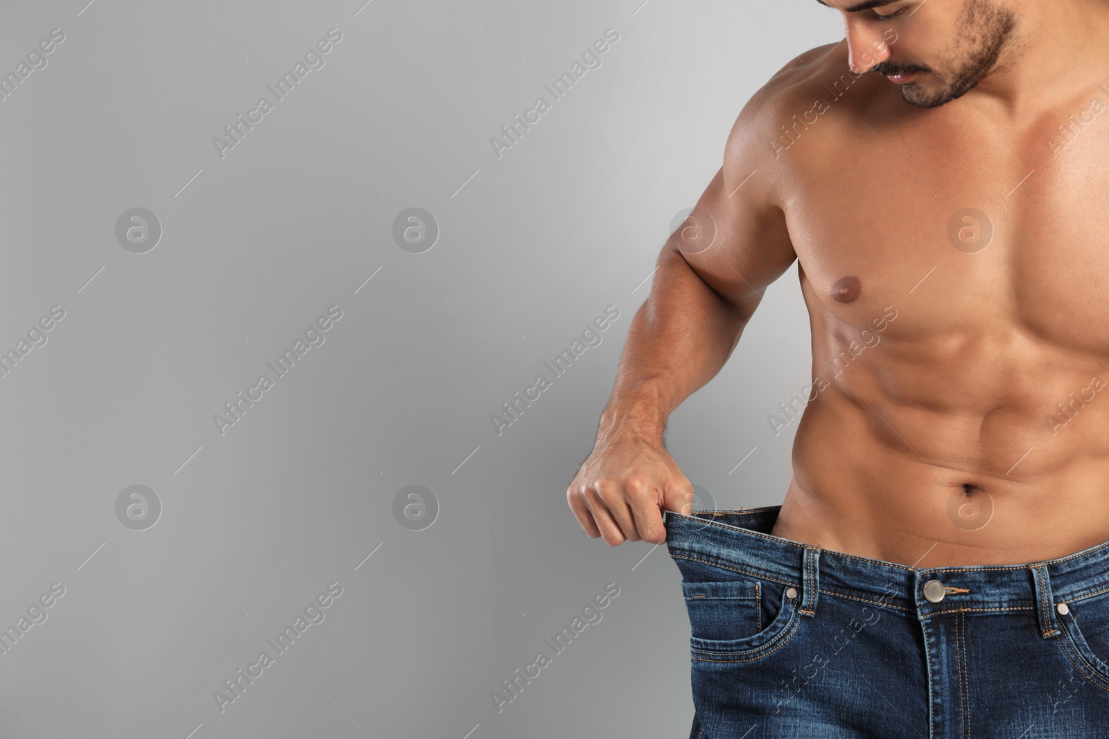 Photo of Young man with slim body in old big size jeans on grey background, closeup view. Space for text