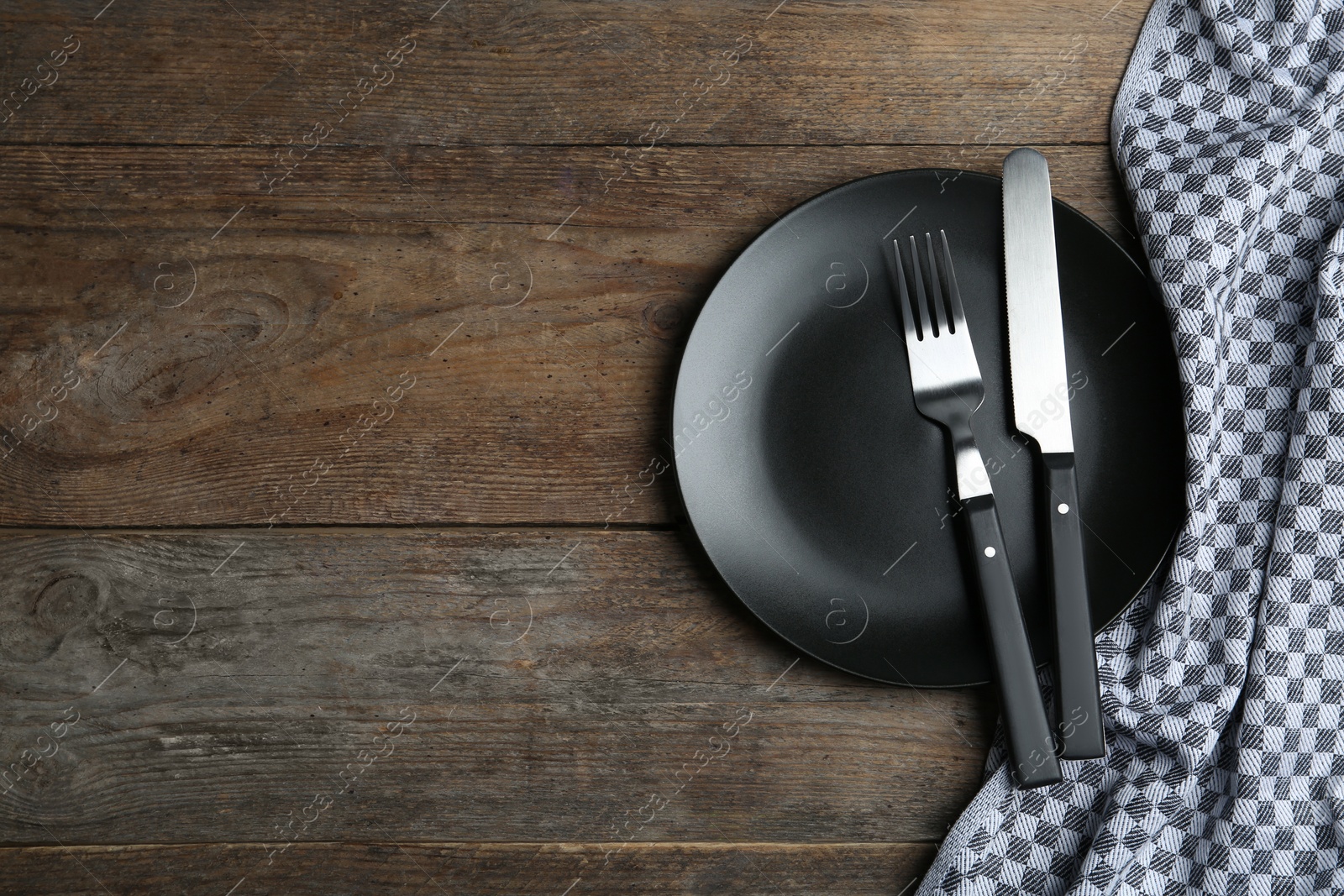 Photo of Empty black plate with cutlery and napkin on wooden table, flat lay. Space for text