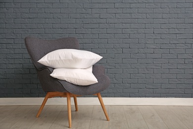 Photo of Pile of soft bed pillows on armchair near brick wall with space for text