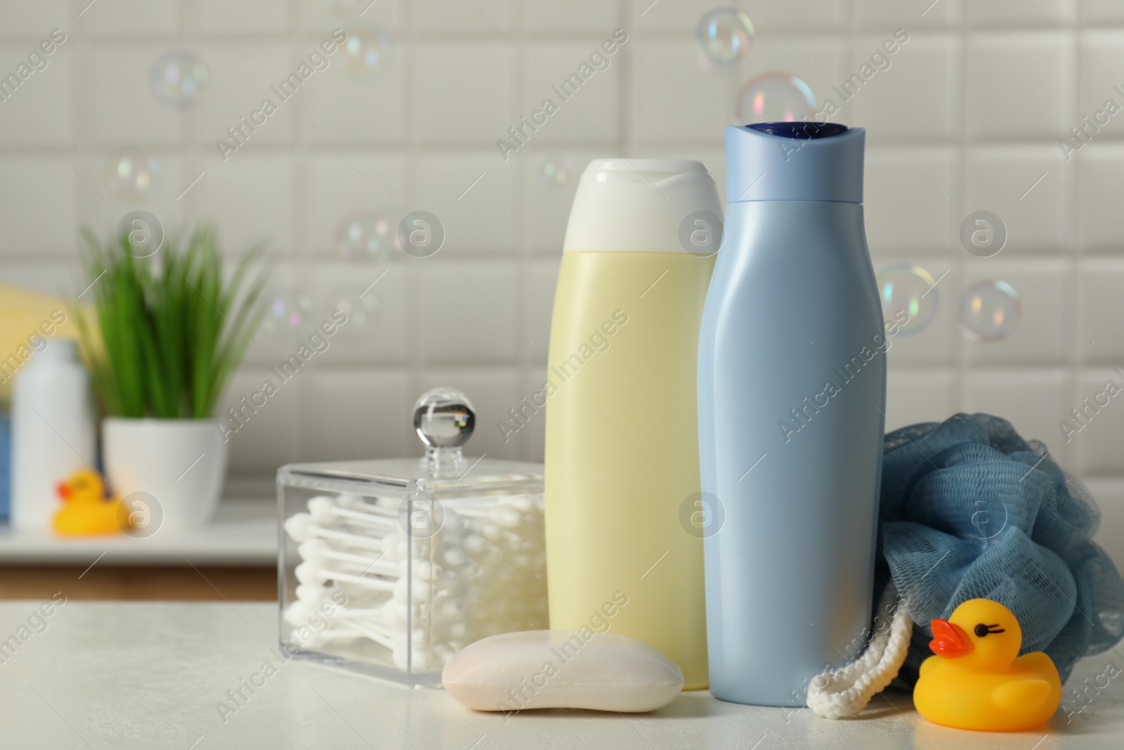 Photo of Baby cosmetic products, bath duck, sponge and cotton swabs on white table against soap bubbles