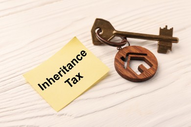 Photo of Inheritance Tax. Paper note and key with key chain in shape of house on white wooden table, closeup