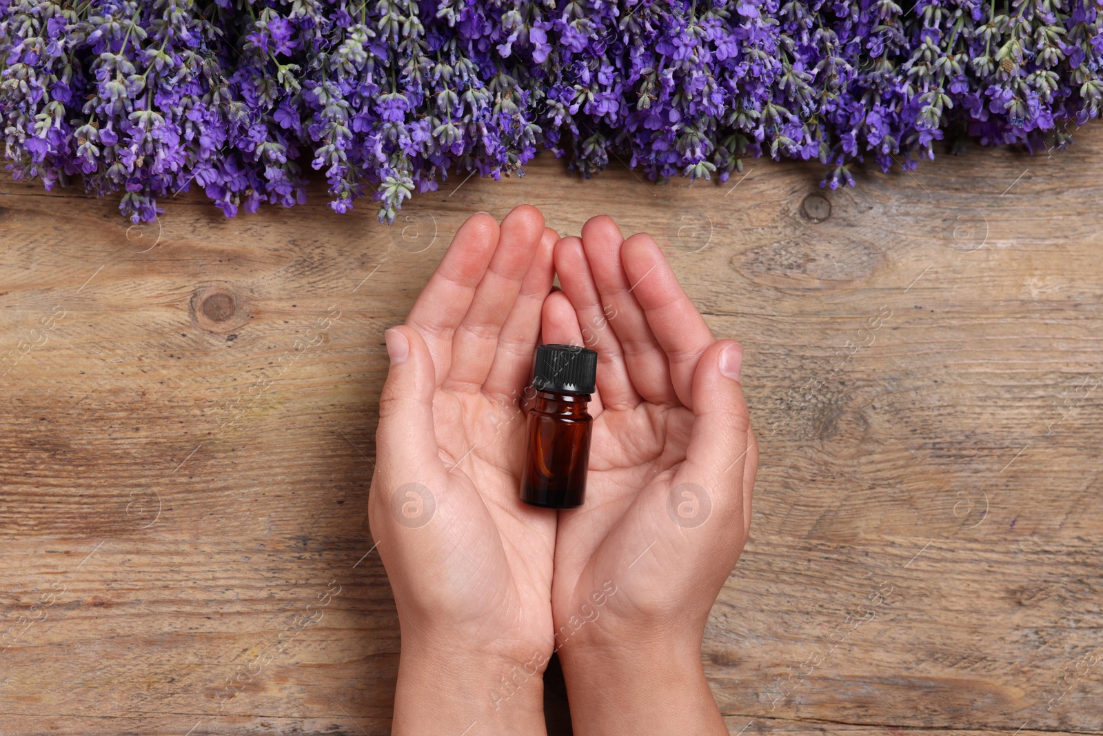 Photo of Woman with bottle of lavender essential oil and flowers on wooden background, top view