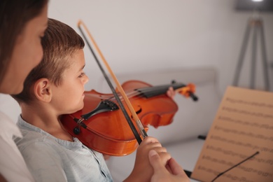 Photo of Young woman teaching little boy to play violin indoors, closeup