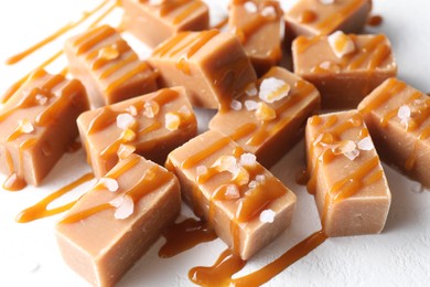 Photo of Tasty candies, caramel sauce and salt on white table, closeup