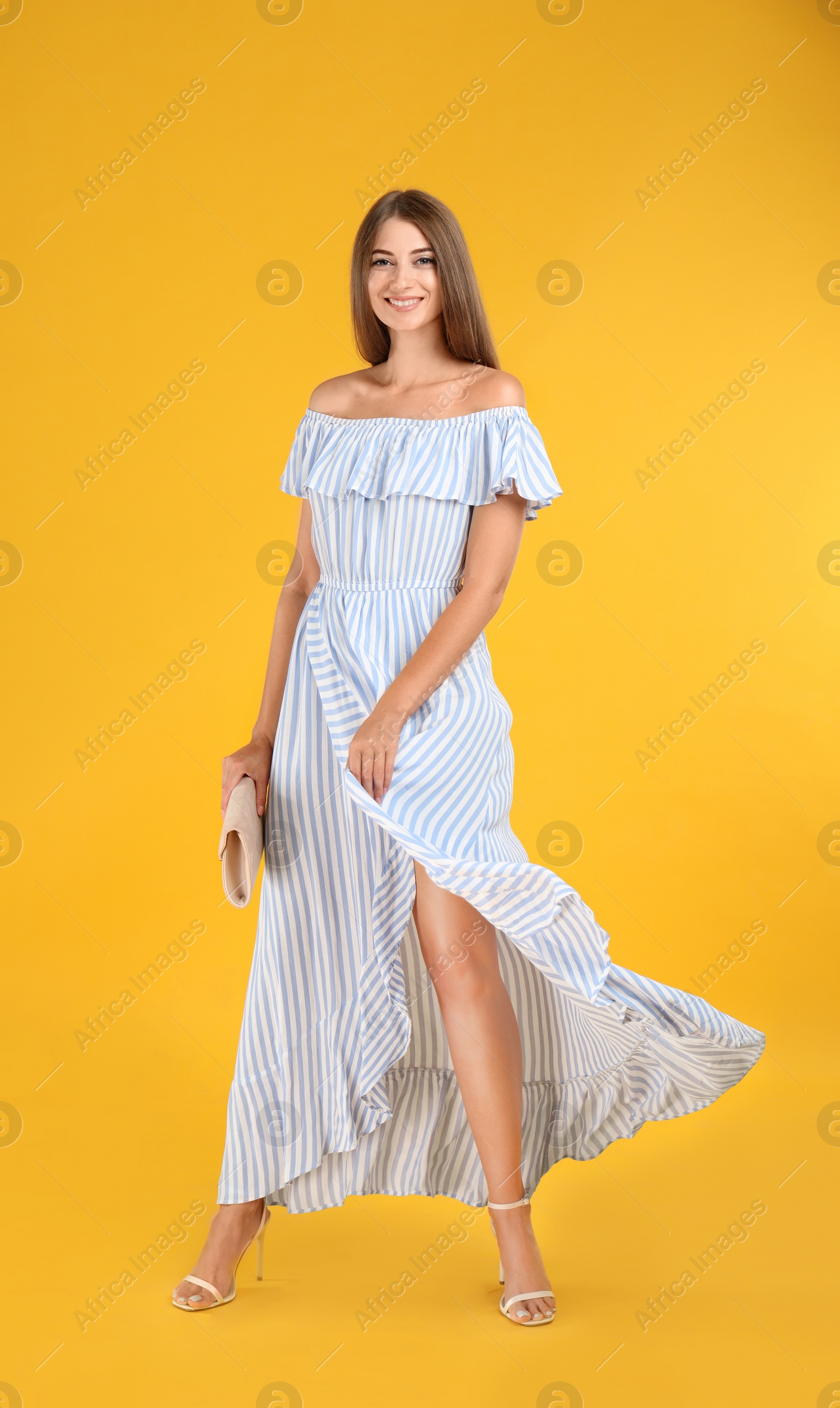 Photo of Young woman wearing stylish dress with elegant clutch on yellow background