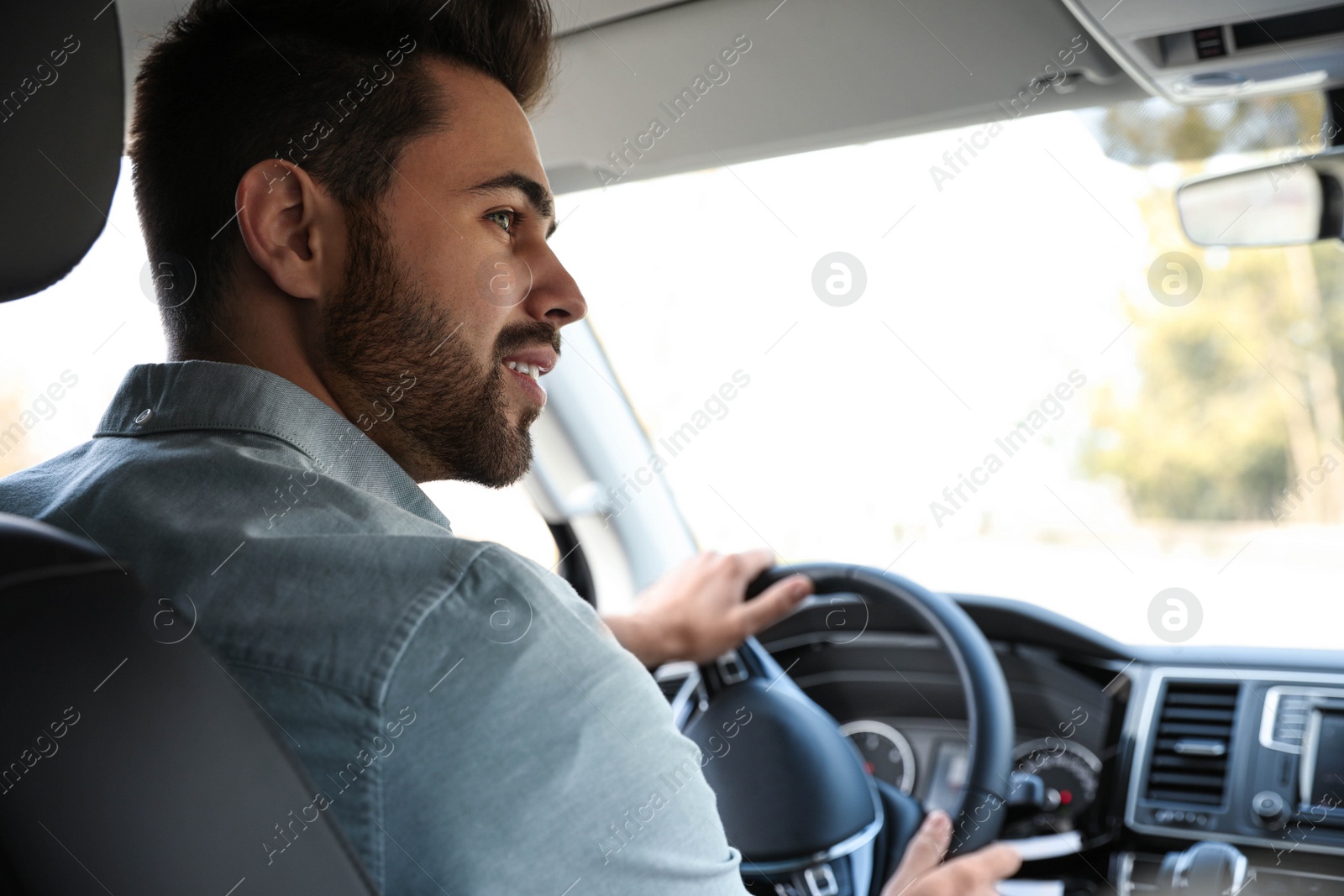 Photo of Handsome young man driving his car, view from backseat