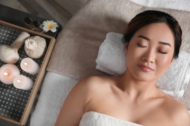 Photo of Beautiful Asian woman lying on massage table in salon, top view