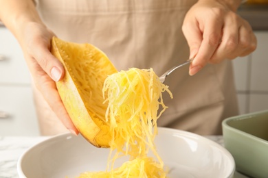 Woman scraping flesh of cooked spaghetti squash with fork in kitchen