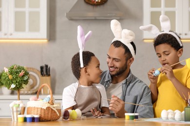 Photo of Happy African American father and his cute children painting Easter eggs at table in kitchen