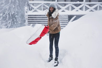 Young woman cleaning snow with shovel near her house