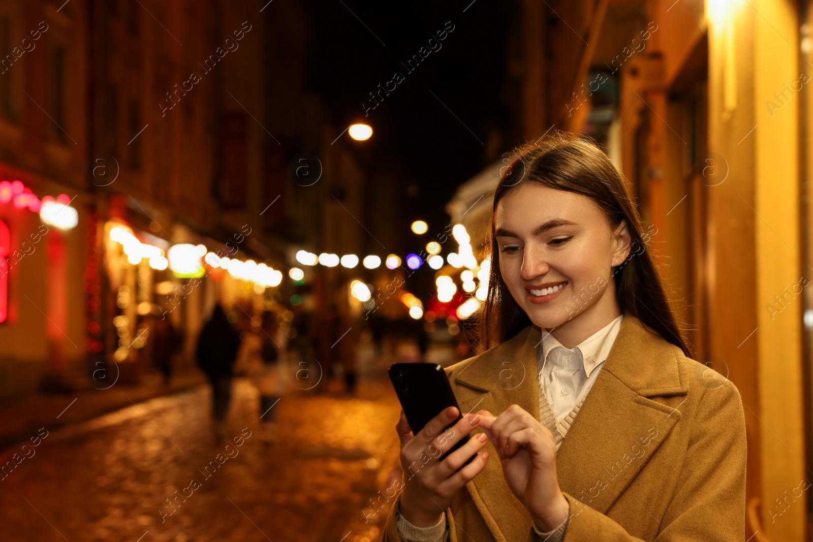 Photo of Smiling woman using smartphone on night city street. Space for text