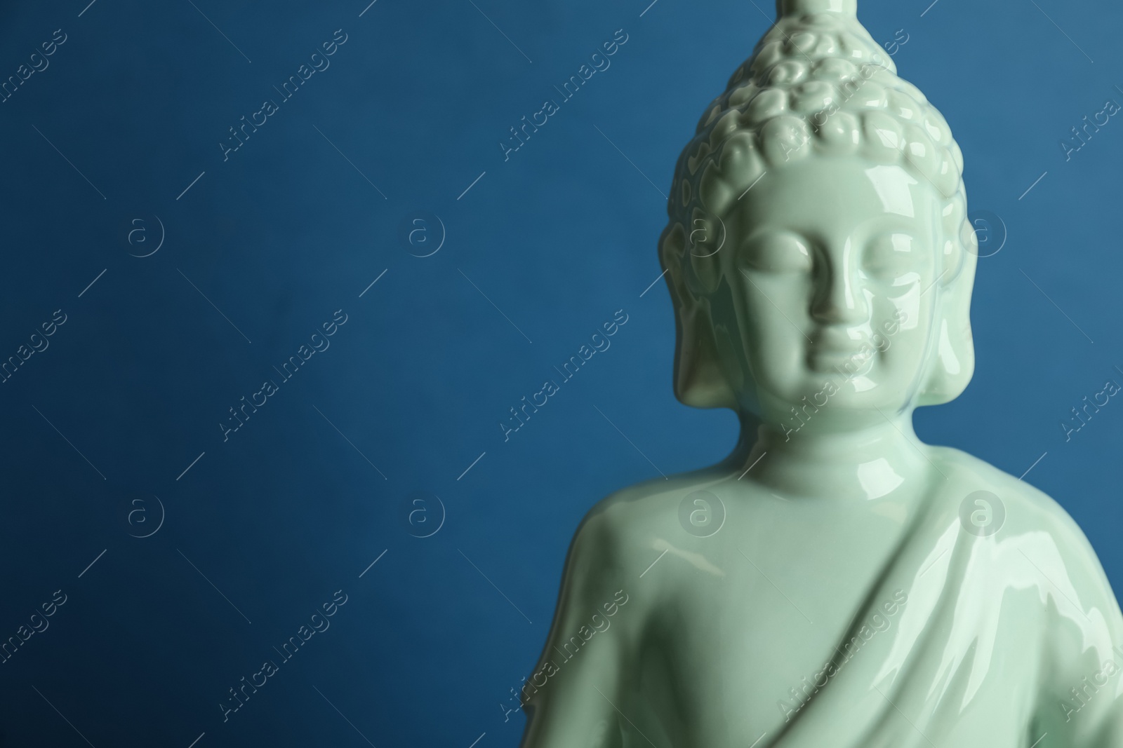 Photo of Beautiful ceramic Buddha sculpture on blue background. Space for text