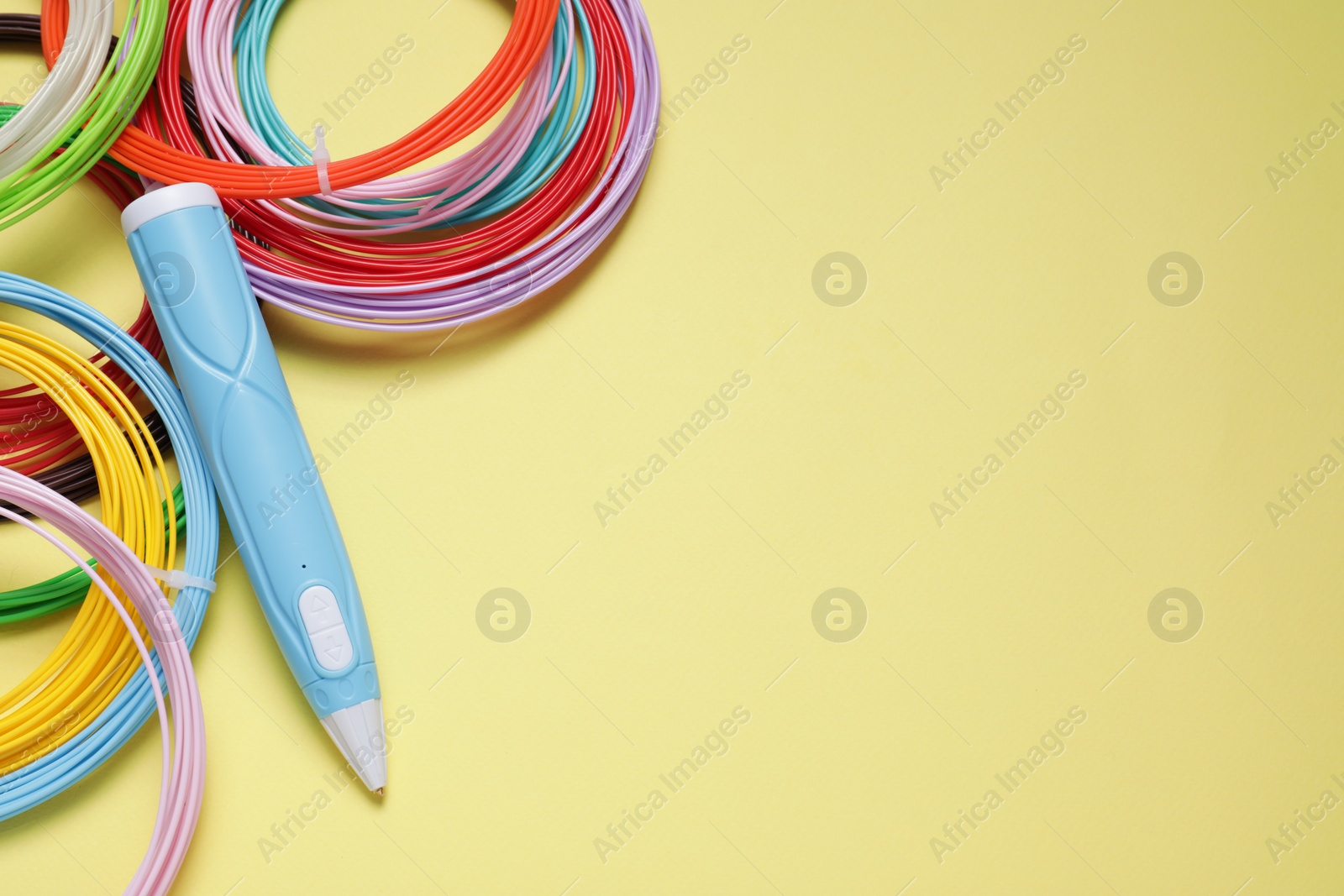 Photo of Stylish 3D pen and colorful plastic filaments on pale yellow background, flat lay. Space for text