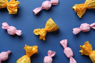 Photo of Many candies in colorful wrappers on blue background, flat lay