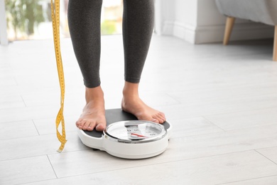 Photo of Woman with tape standing on scales indoors, space for text. Overweight problem