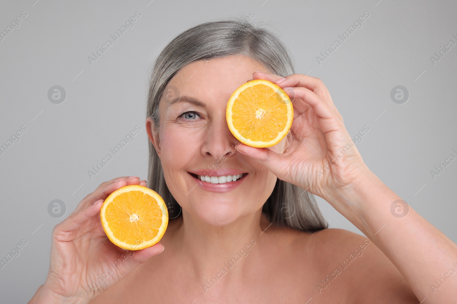 Photo of Beautiful woman with halves of orange rich in vitamin C on grey background