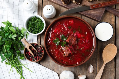 Photo of Stylish brown clay bowl with Ukrainian borsch on wooden table, flat lay