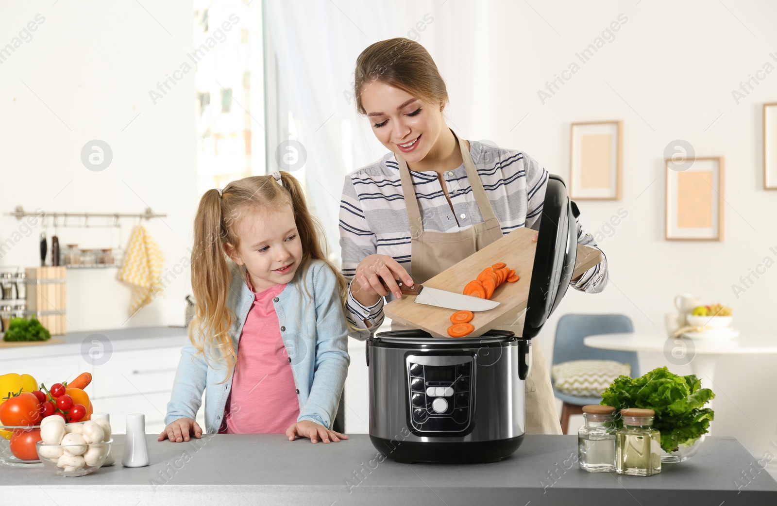 Photo of Mother and daughter preparing food with modern multi cooker in kitchen