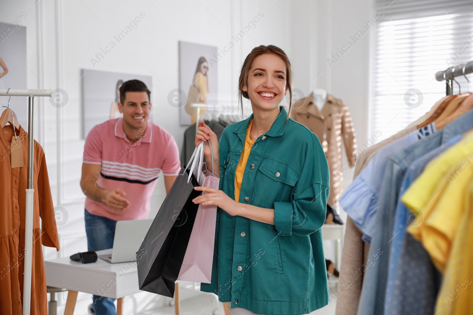 Photo of Young woman holding shopping bags near rack with clothes in modern boutique