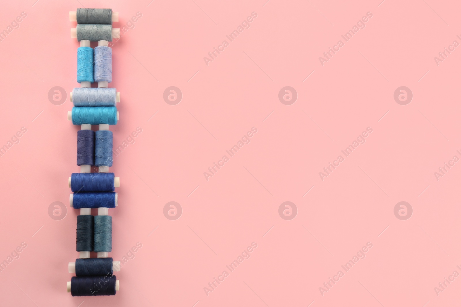 Photo of Different shades of blue sewing threads on pink background, flat lay. Space for text