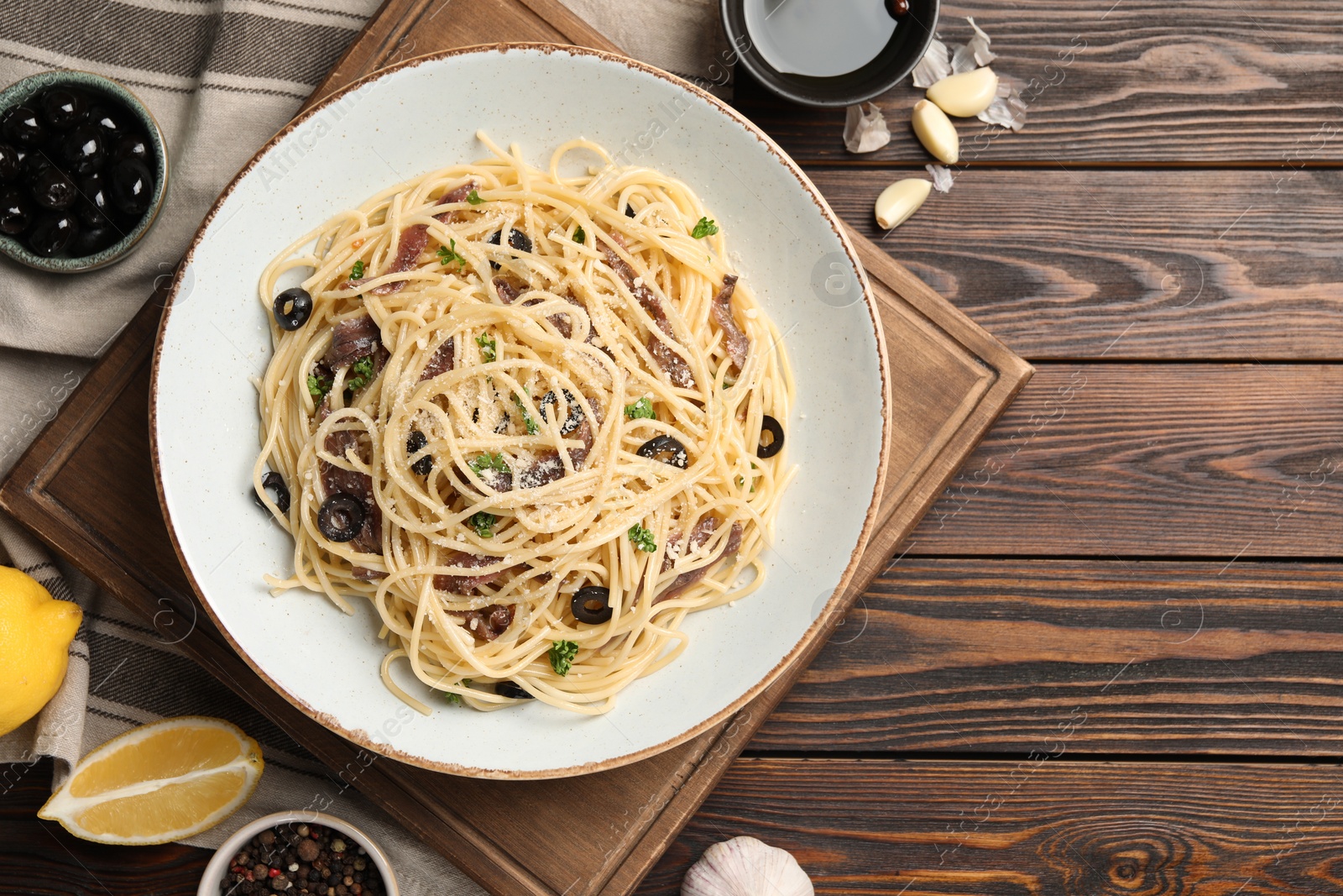 Photo of Delicious pasta with anchovies, olives and parmesan cheese served on wooden table, flat lay. Space for text