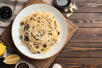 Delicious pasta with anchovies, olives and parmesan cheese served on wooden table, flat lay. Space for text