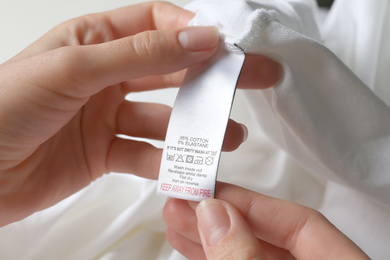 Photo of Woman reading clothing label with care symbols and material content on white shirt, closeup